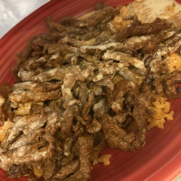 La Fiesta Mexican's steak and rice dish, topped with a creamy white sauce, served on a red plate.