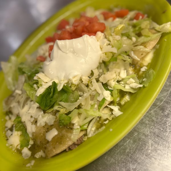La Fiesta Mexican enchiladas topped with lettuce, tomatoes, cheese, and sour cream on a lime green plate.