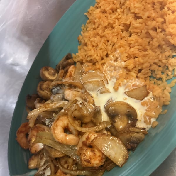 Shrimp and mushrooms in a creamy sauce with onions, served with Mexican rice on a blue plate.
